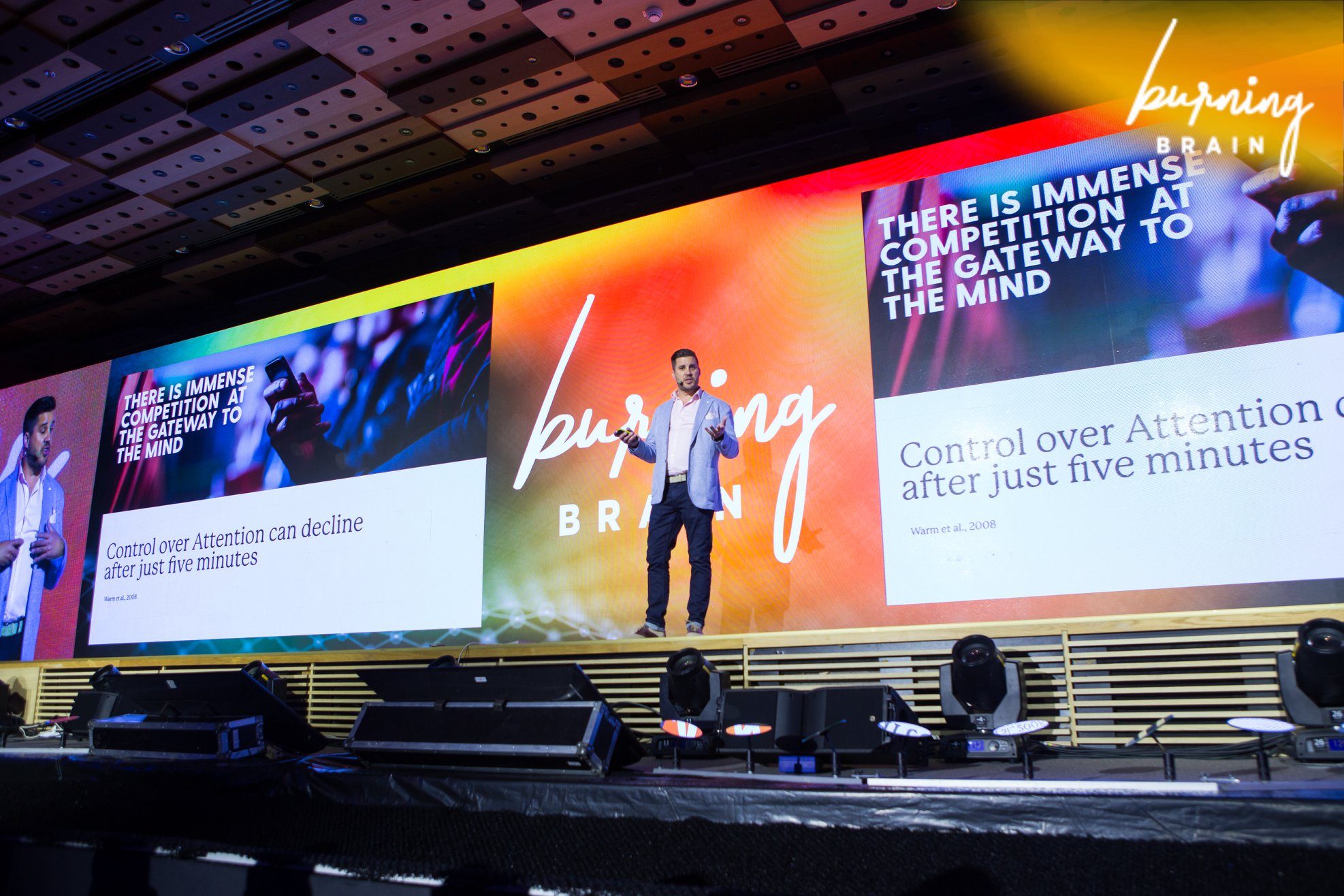 Ben Moorsom on a large stage, the screens behind him reading: there is immense competition at the gateway to the mind
